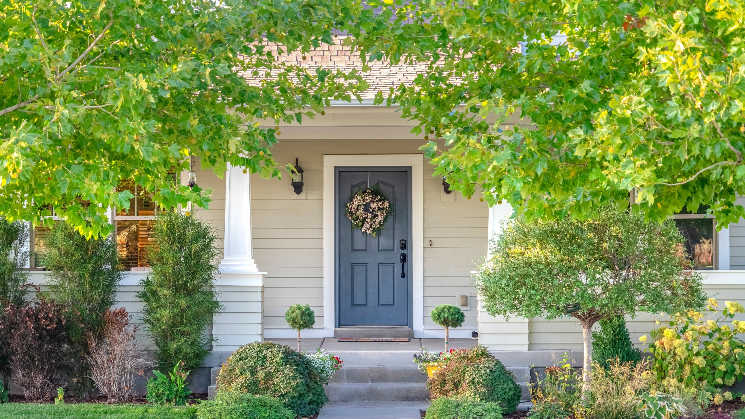 Front entryway of home with blue door and leafy green summer foliage