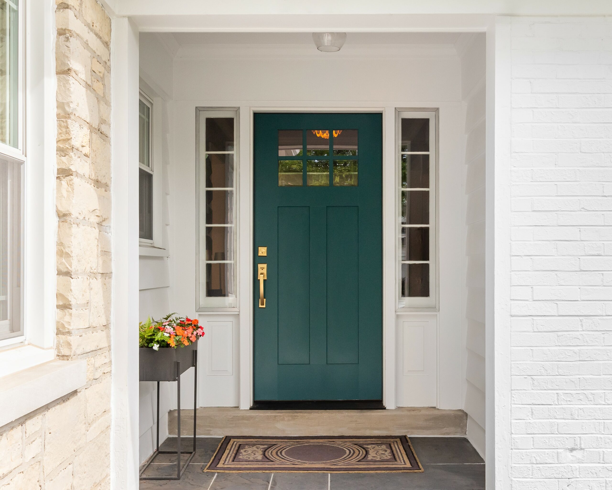Dark green-blue front door on porch of house with white siding and stone walkway