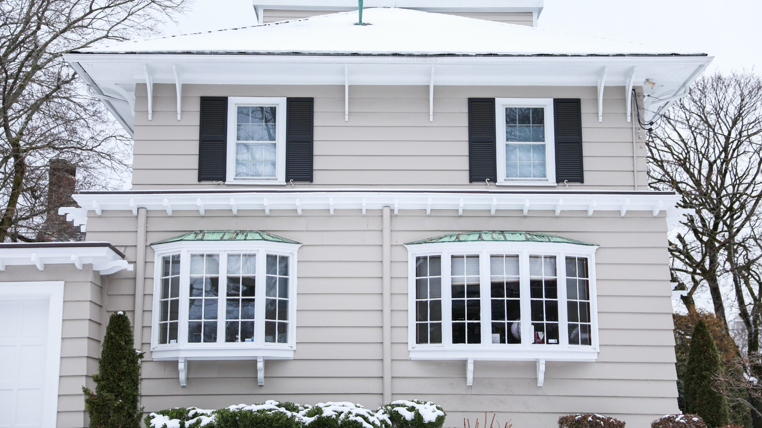 Home exterior with large bow and bay windows on first floor and smaller windows with black shutters on the second floor