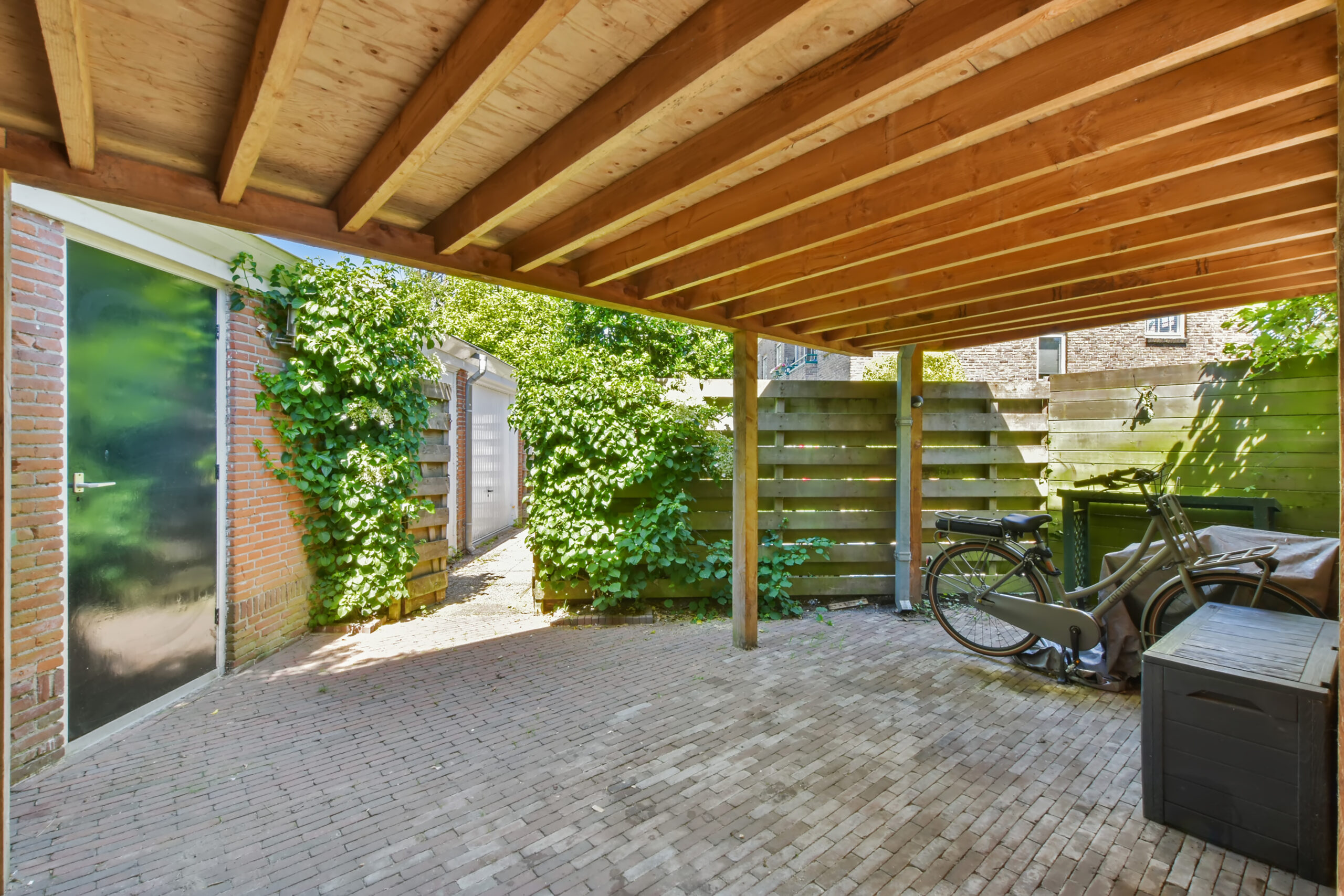 Wood patio enclosure outside of a brick home with a bicycle and boxes