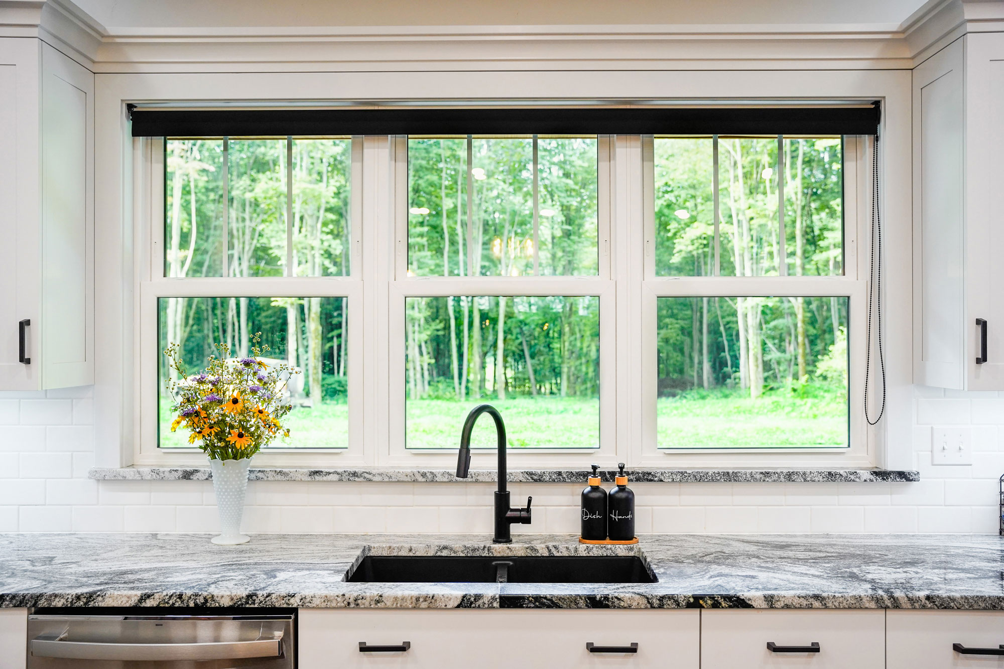 Double-hung windows above a black sink and marble countertop in a kitchen, looking outside